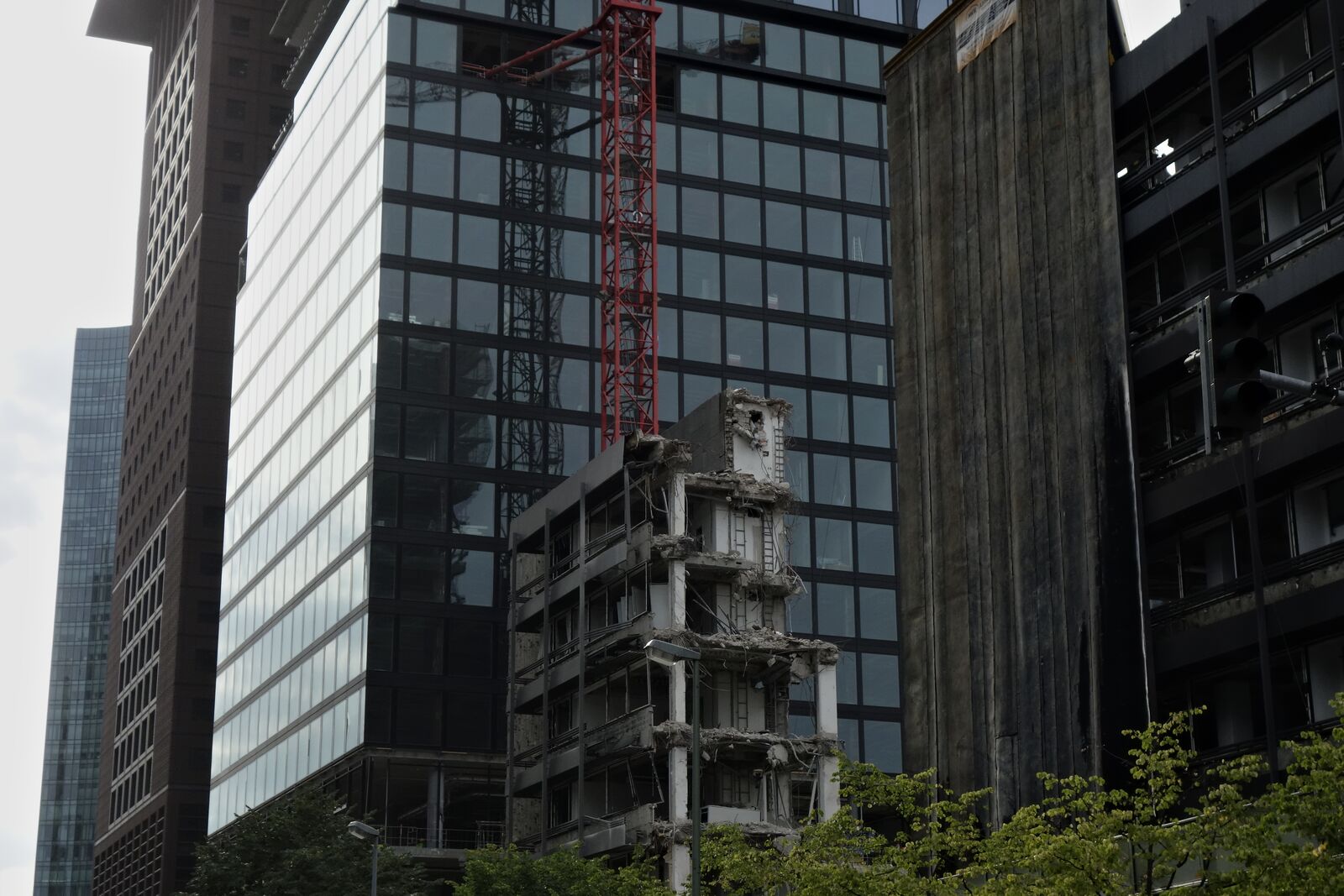 Photograph: demolition of a skyscraper or large office building. Only the last stump is left. The scene is very dark (all buildings are black), and ominous. There's a dark red construction crane and a multi-story tarp hanging from the adjacent building.